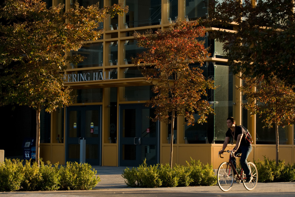 Student biking in front of the Engineering building two faculty members