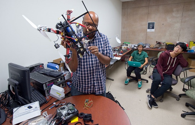 professor adjusts a drone as two students watch academic initiatives call